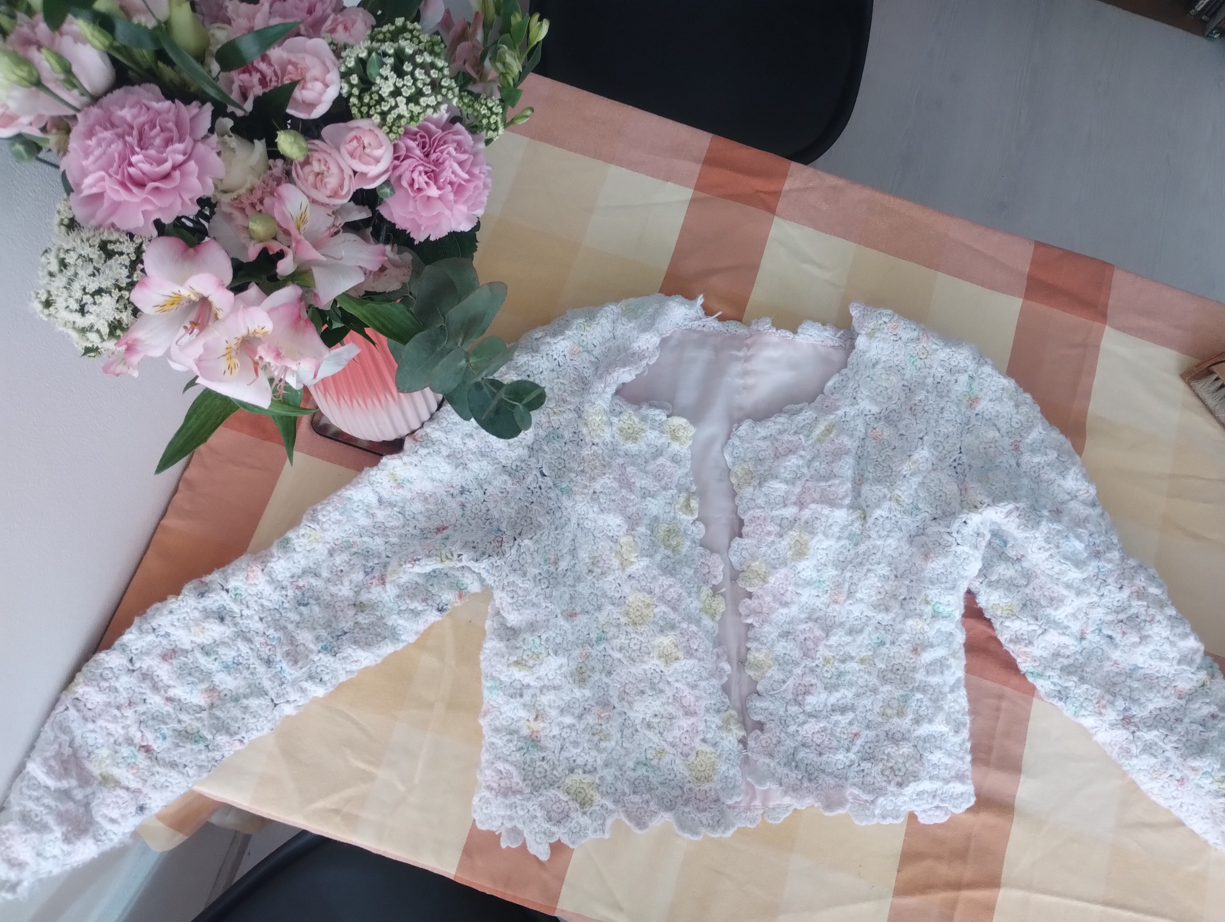 A cardigan covered in small crocheted flowers made from speckled white scrap yarn