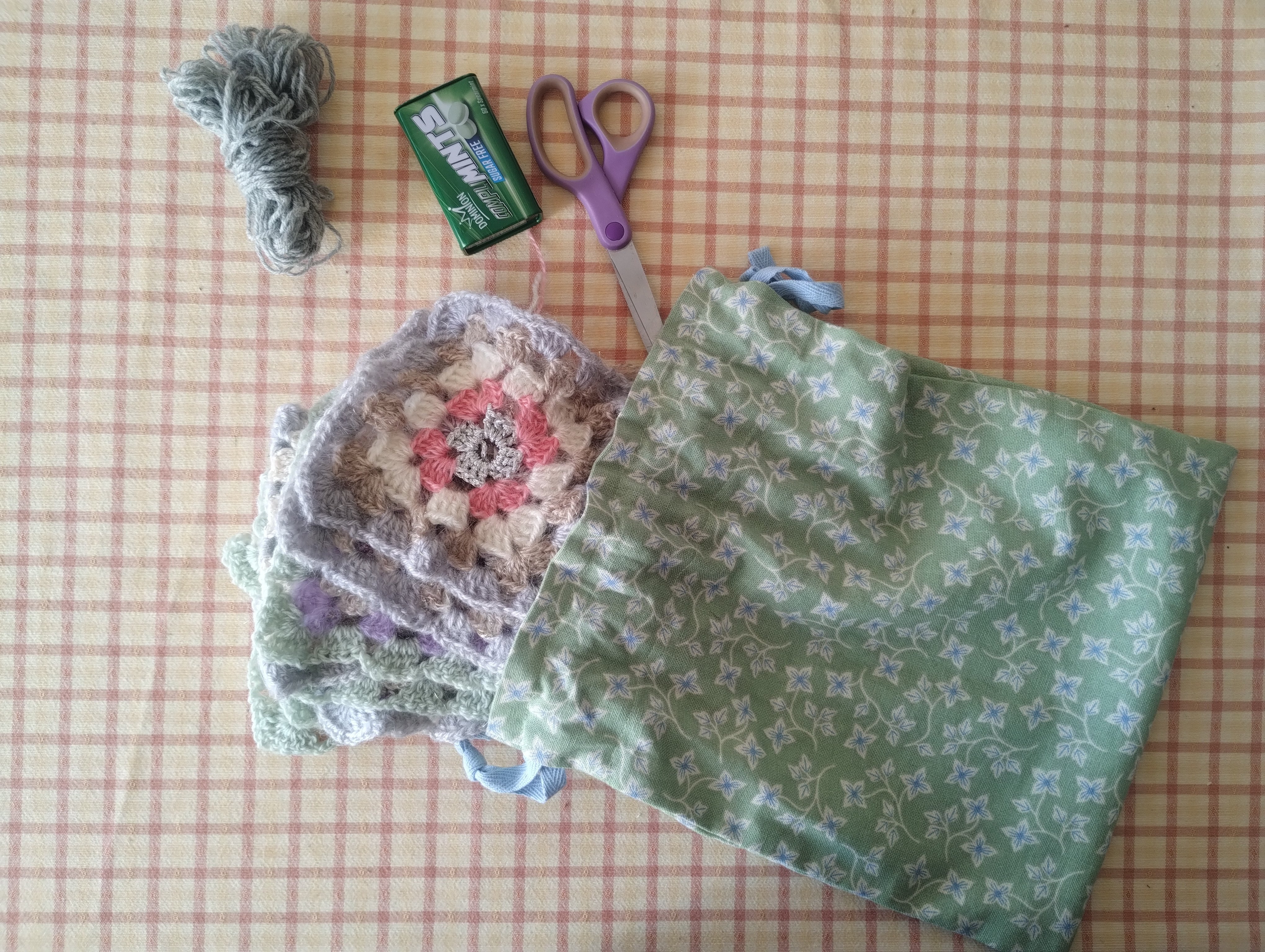 A drawstring bag holding granny square crochet, yarn, and scissors