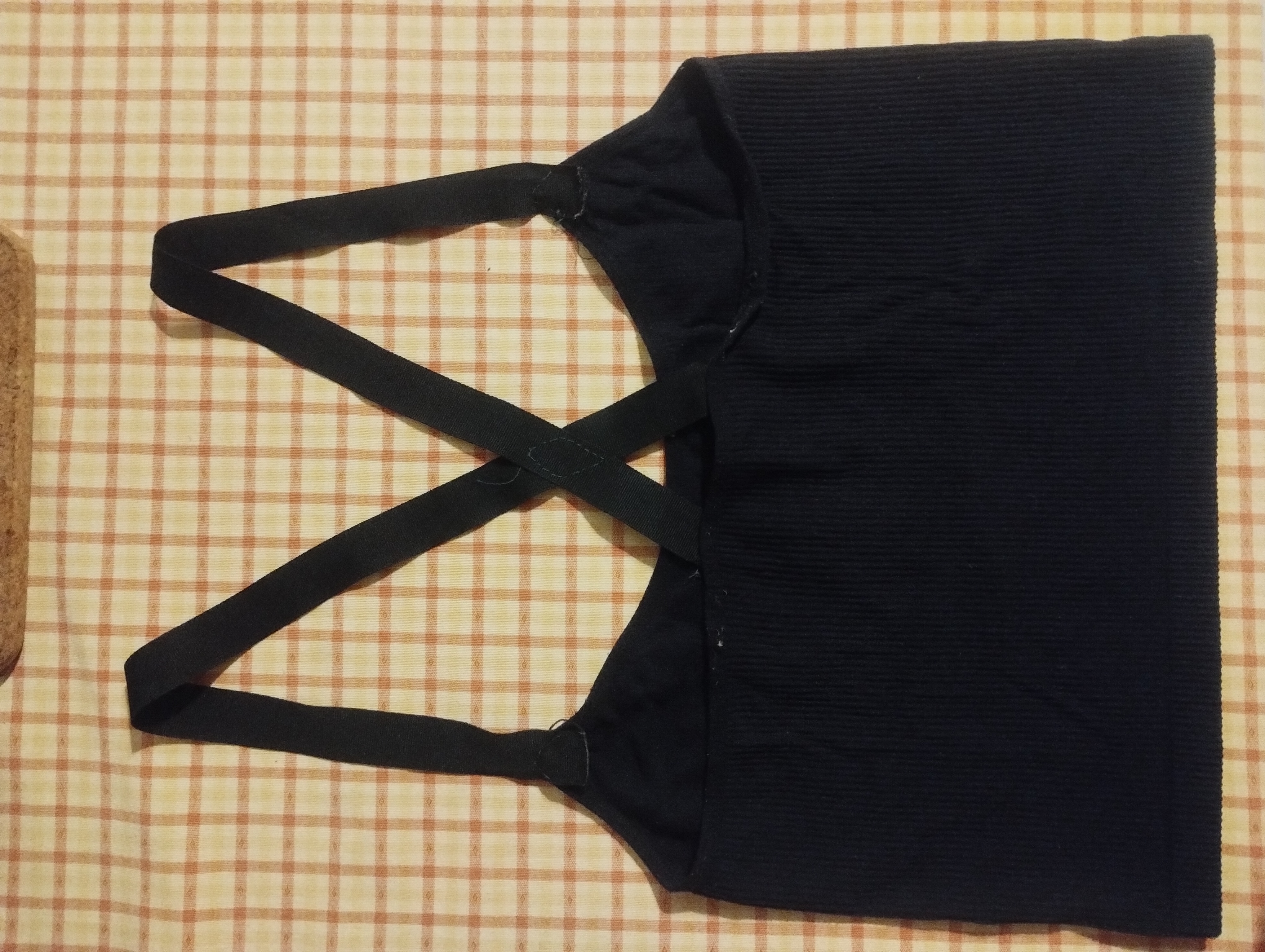 The back of a black crop top with crossed elastic straps between the shoulder blades