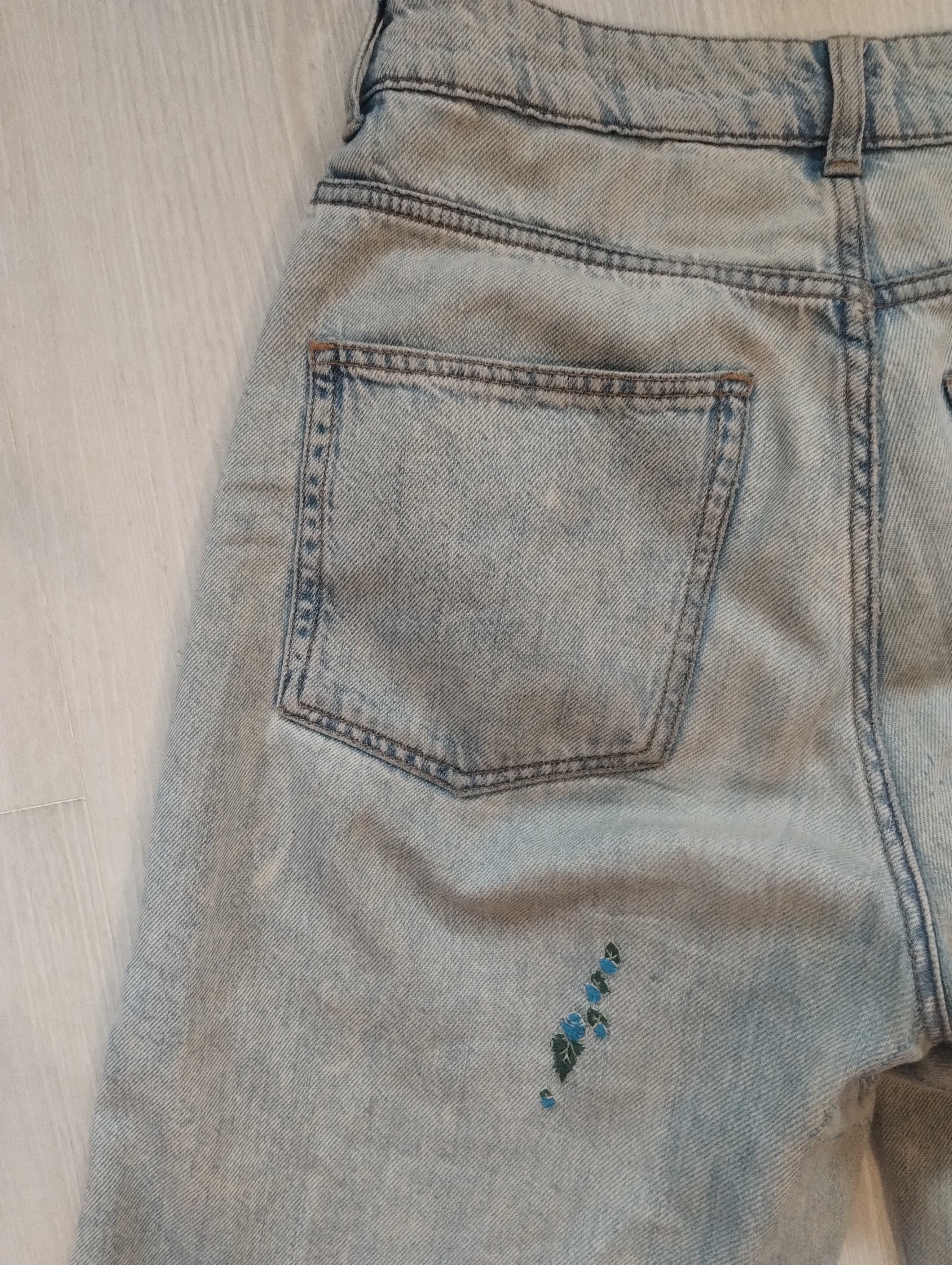 The back pocket of light-wash jeans embroidered with small blue roses