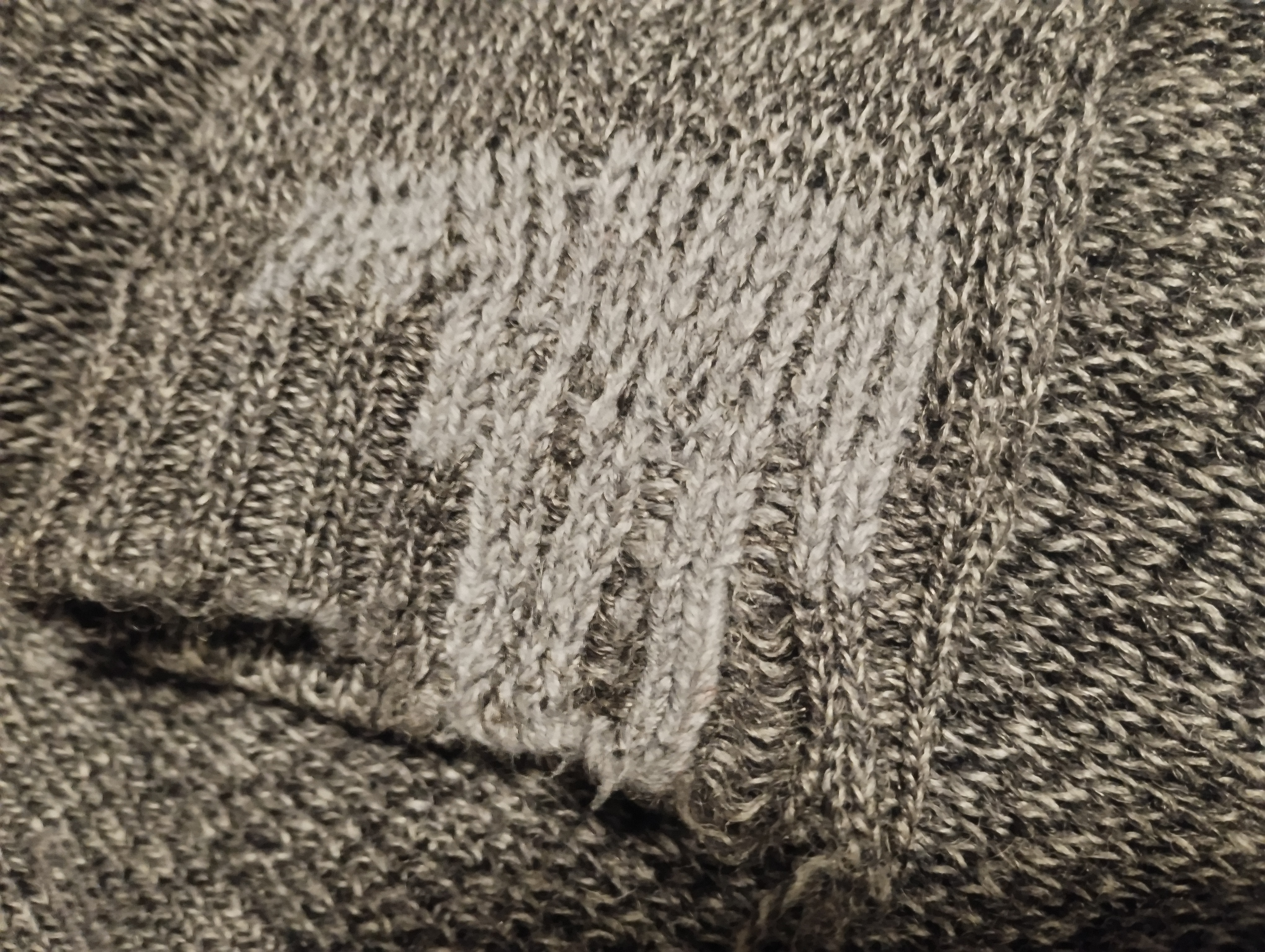 Close-up of a grey jumper cuff repaired with a visible mending patch