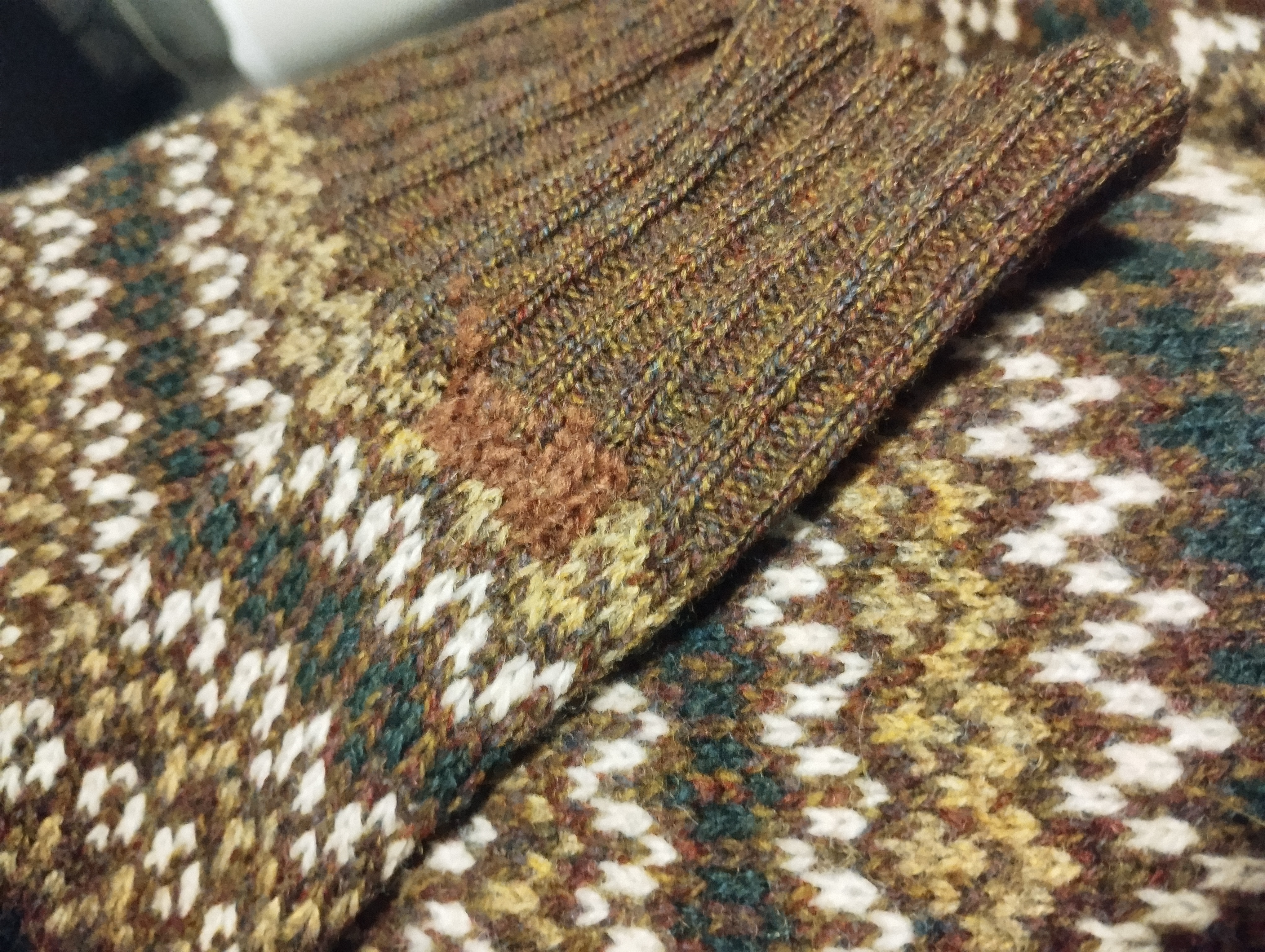 Close-up of a fair isle patterned cuff mended with a patch of rust-coloured wool