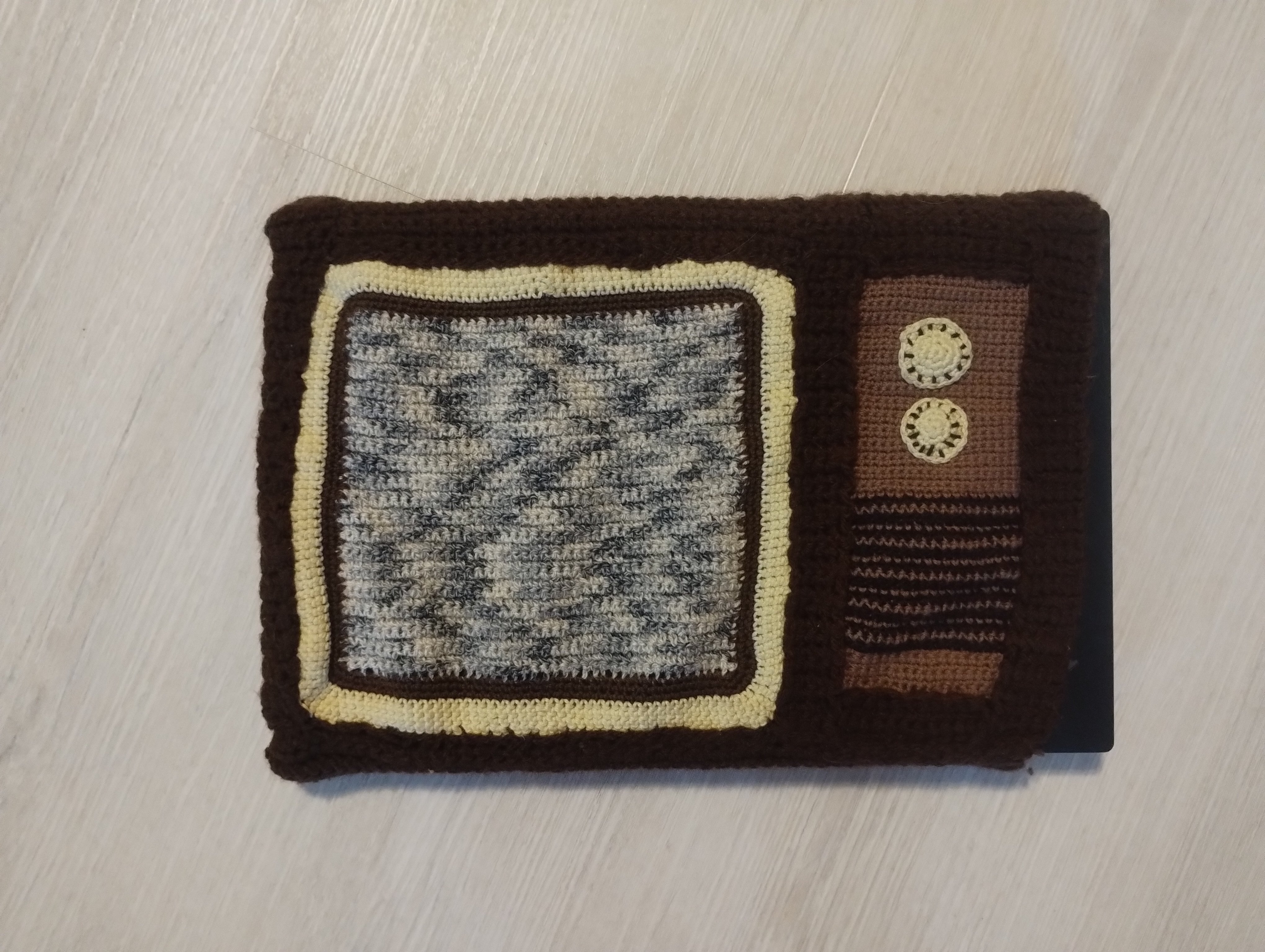 A laptop sleeve crocheted to look like an old television, with static on the screen and two dial buttons on the side