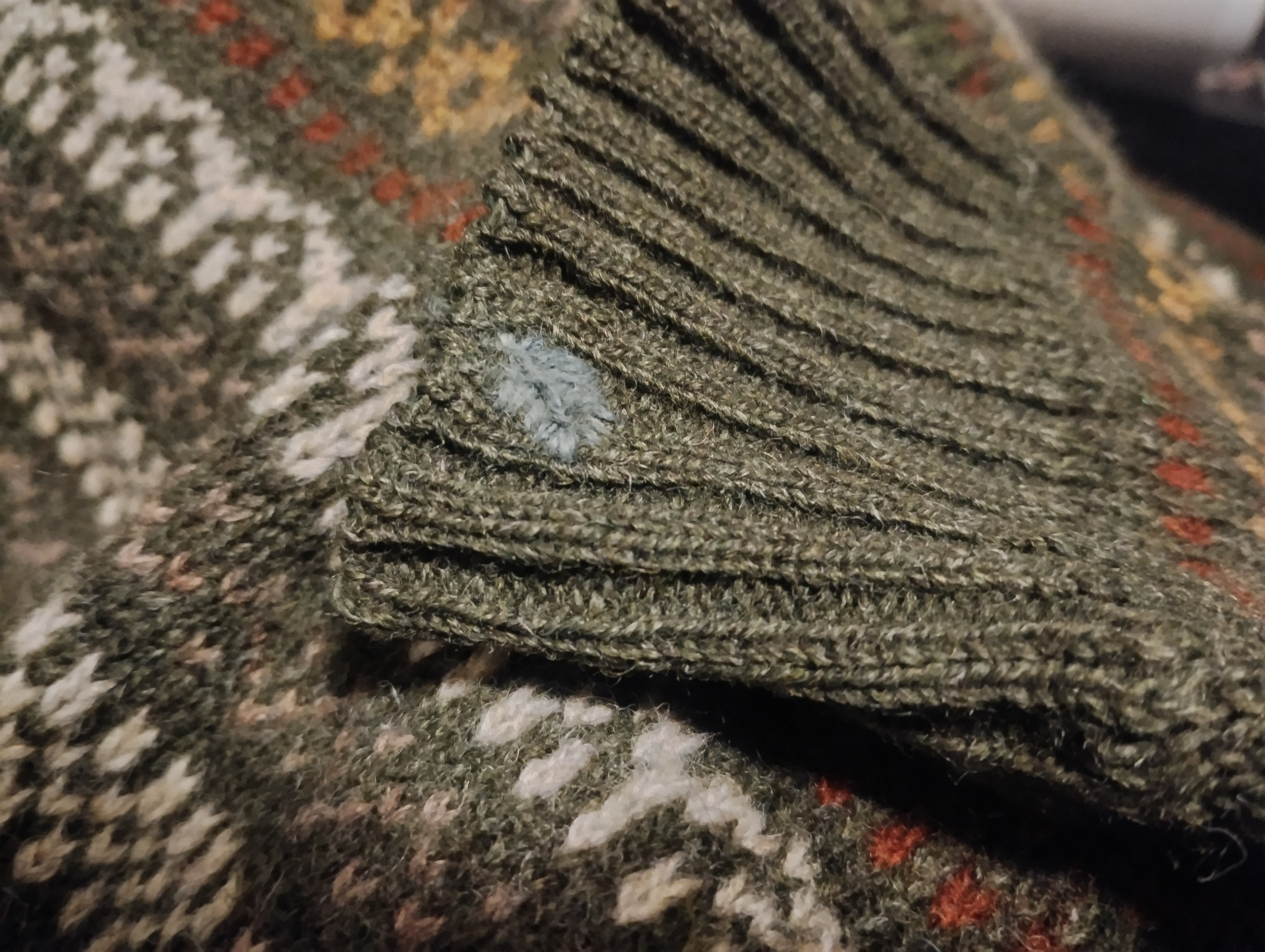 Close-up of ribbed olive knitwear mended with a small blue-grey leaf-shaped patch