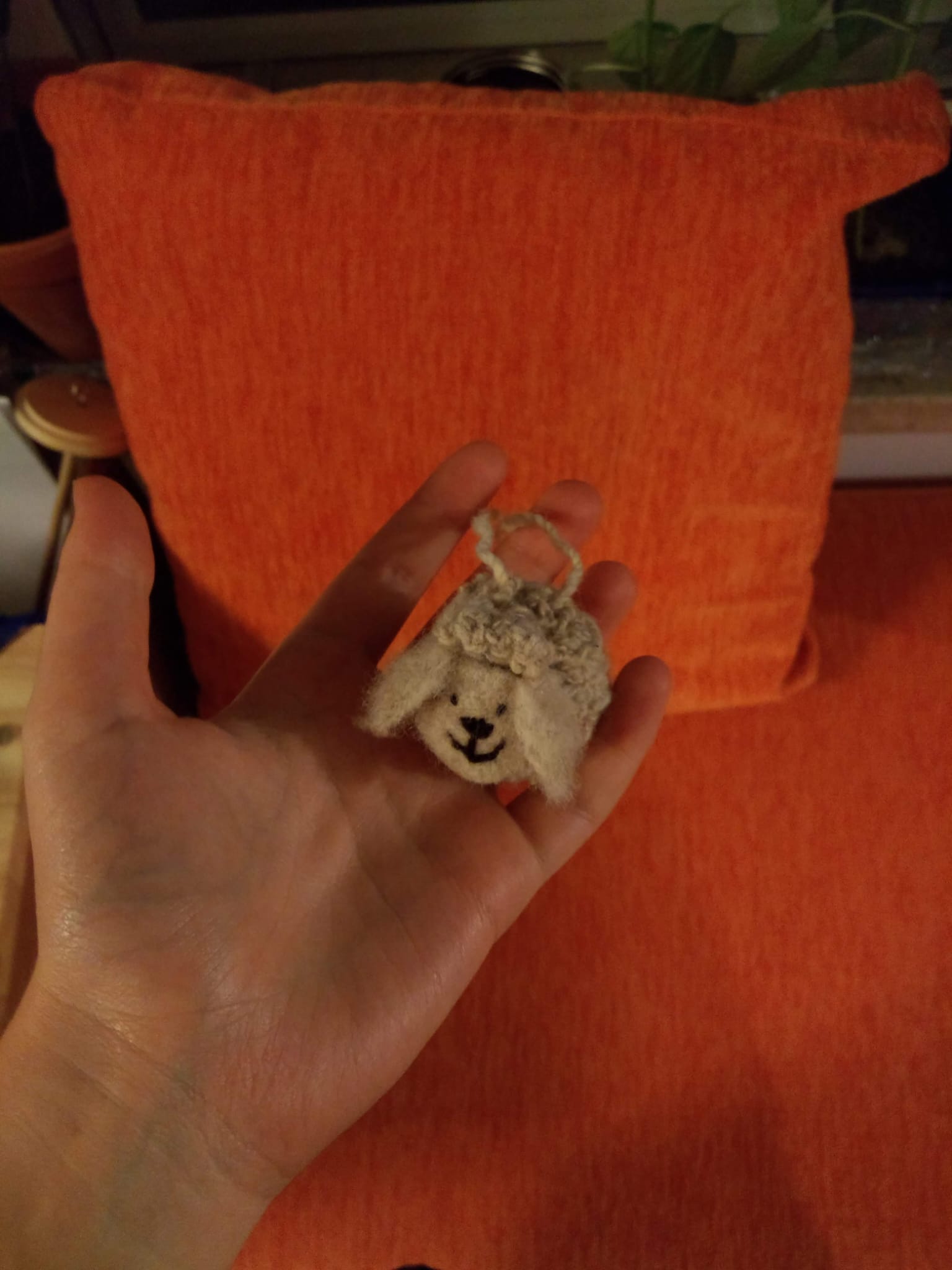 A tiny needle-felted sheep face charm held between two fingers