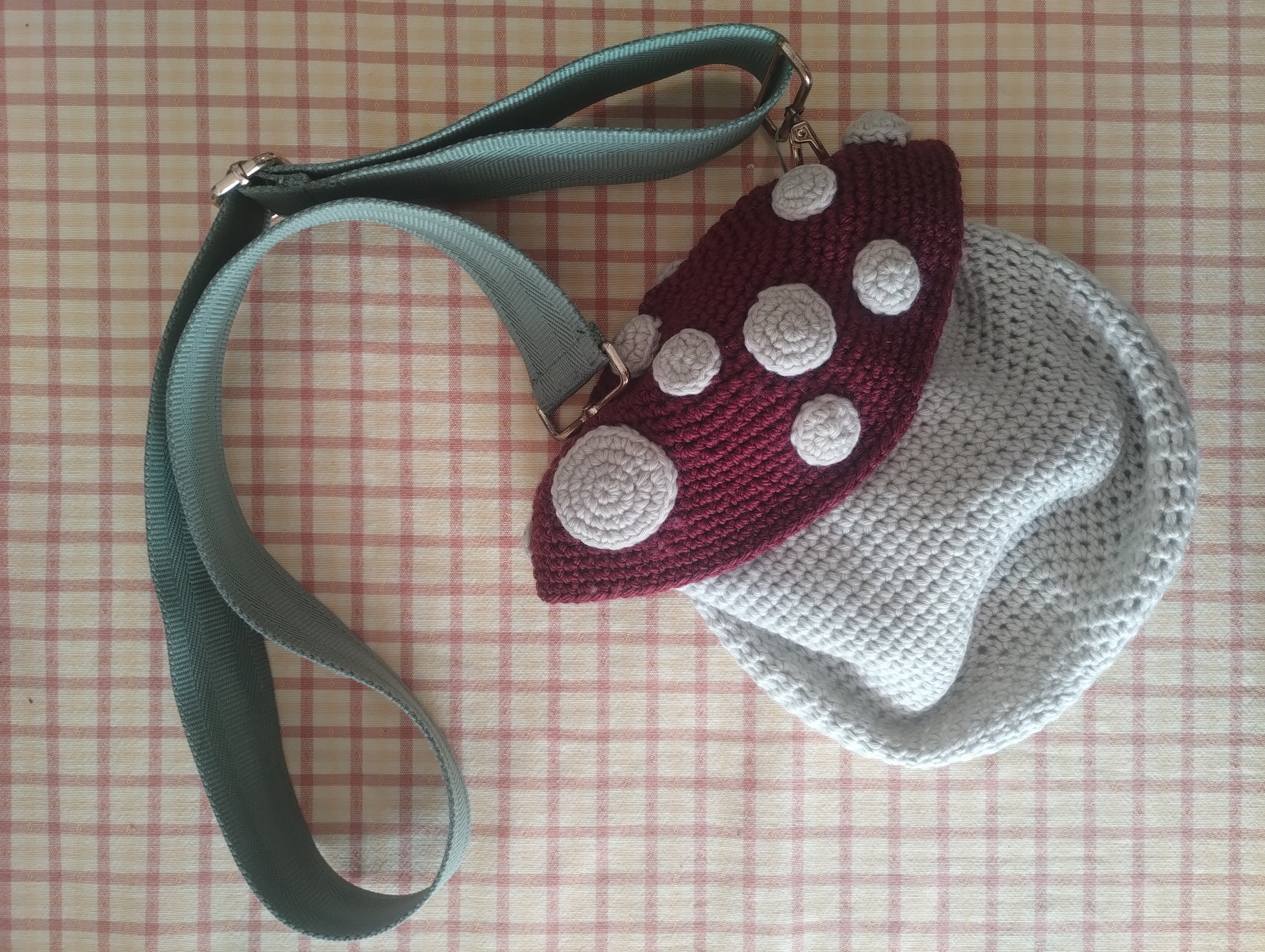A crocheted toadstool-shaped bag with a red spotted cap and a mint green strap