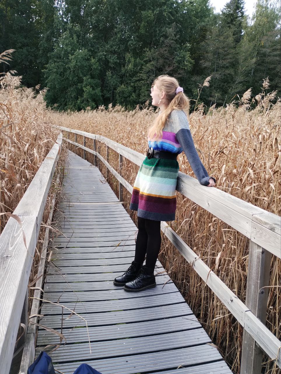 A striped colour-block jumper belted at the waist and worn as a dress on a boardwalk through reed beds