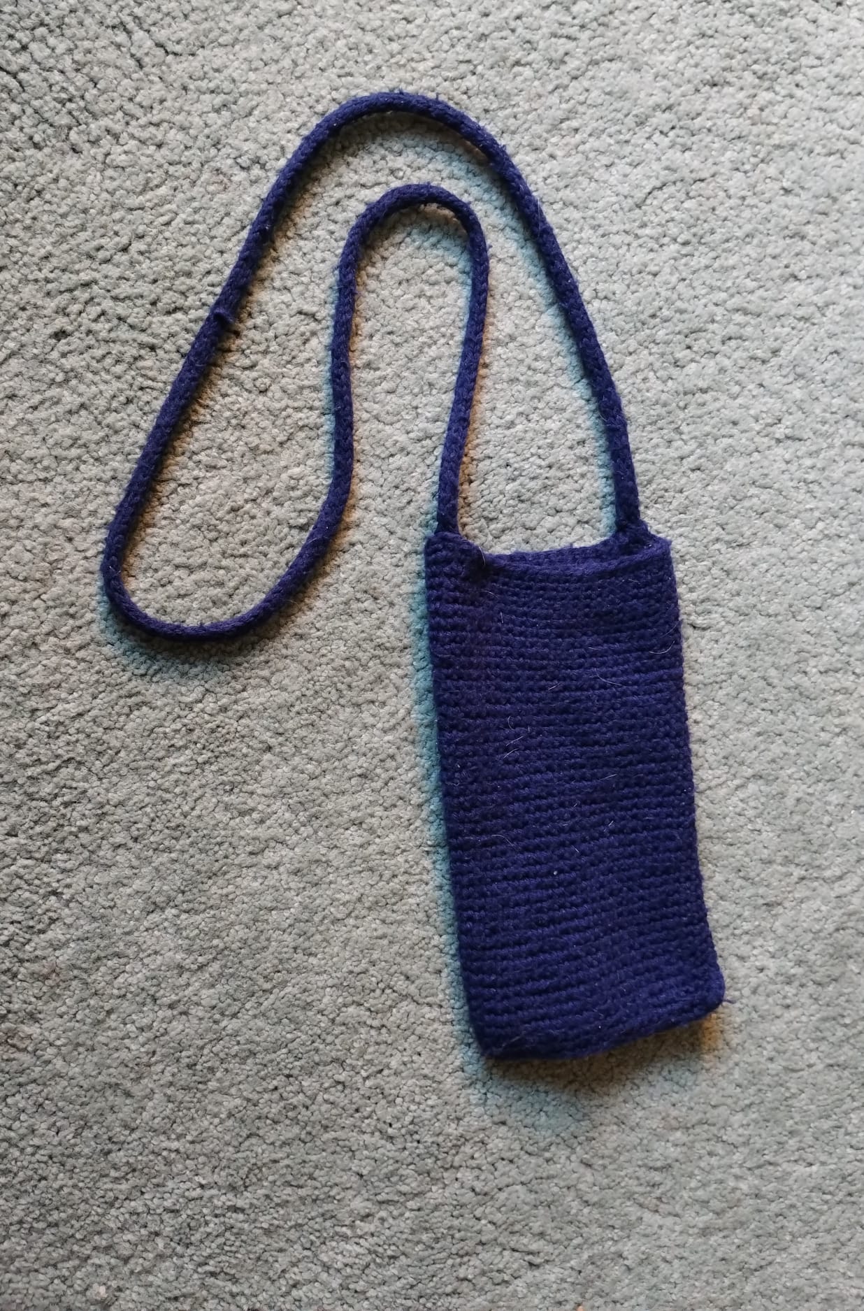 A navy crocheted phone pouch on a long crossbody strap