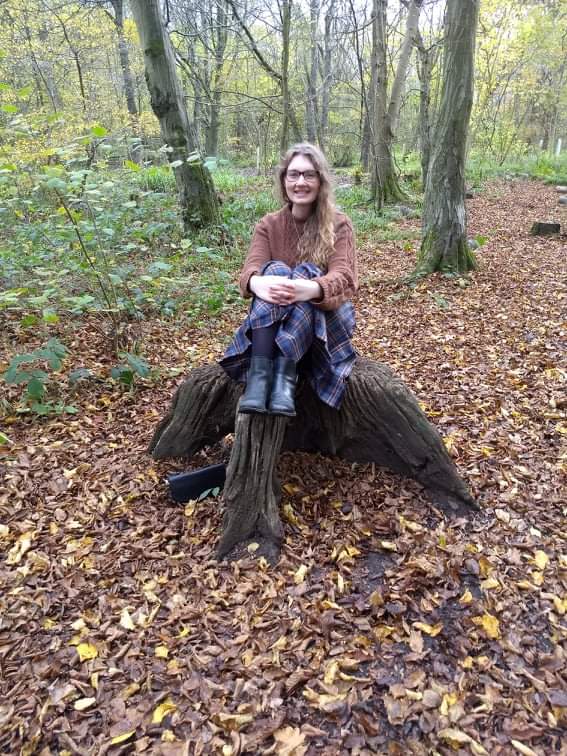 Joanna sitting on a tree stump in the woods
