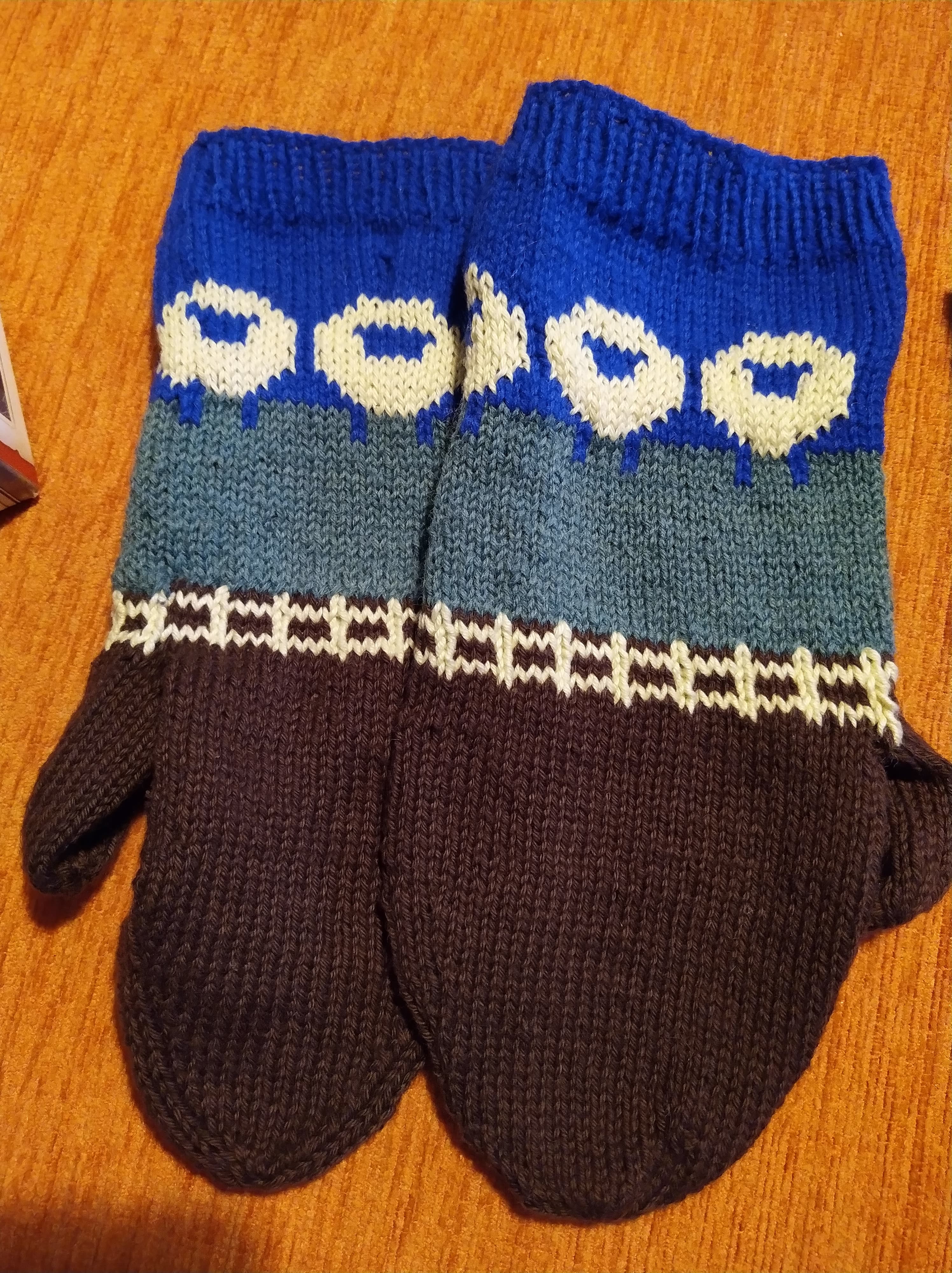 A pair of hand-knitted mittens with a sheep pattern
