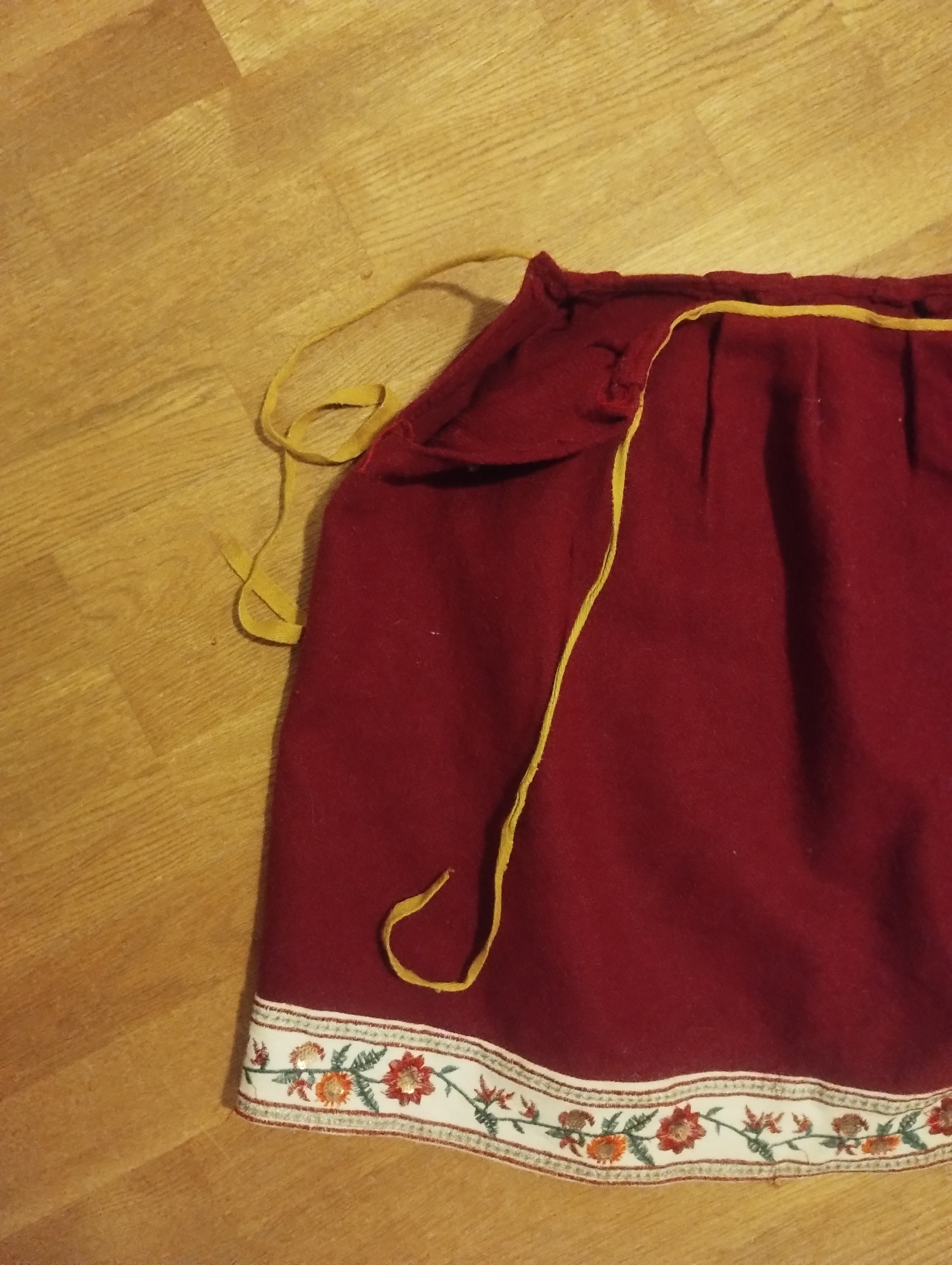A red wool skirt with a mustard drawstring gathered at the waistband and a cream floral ribbon trim along the hem