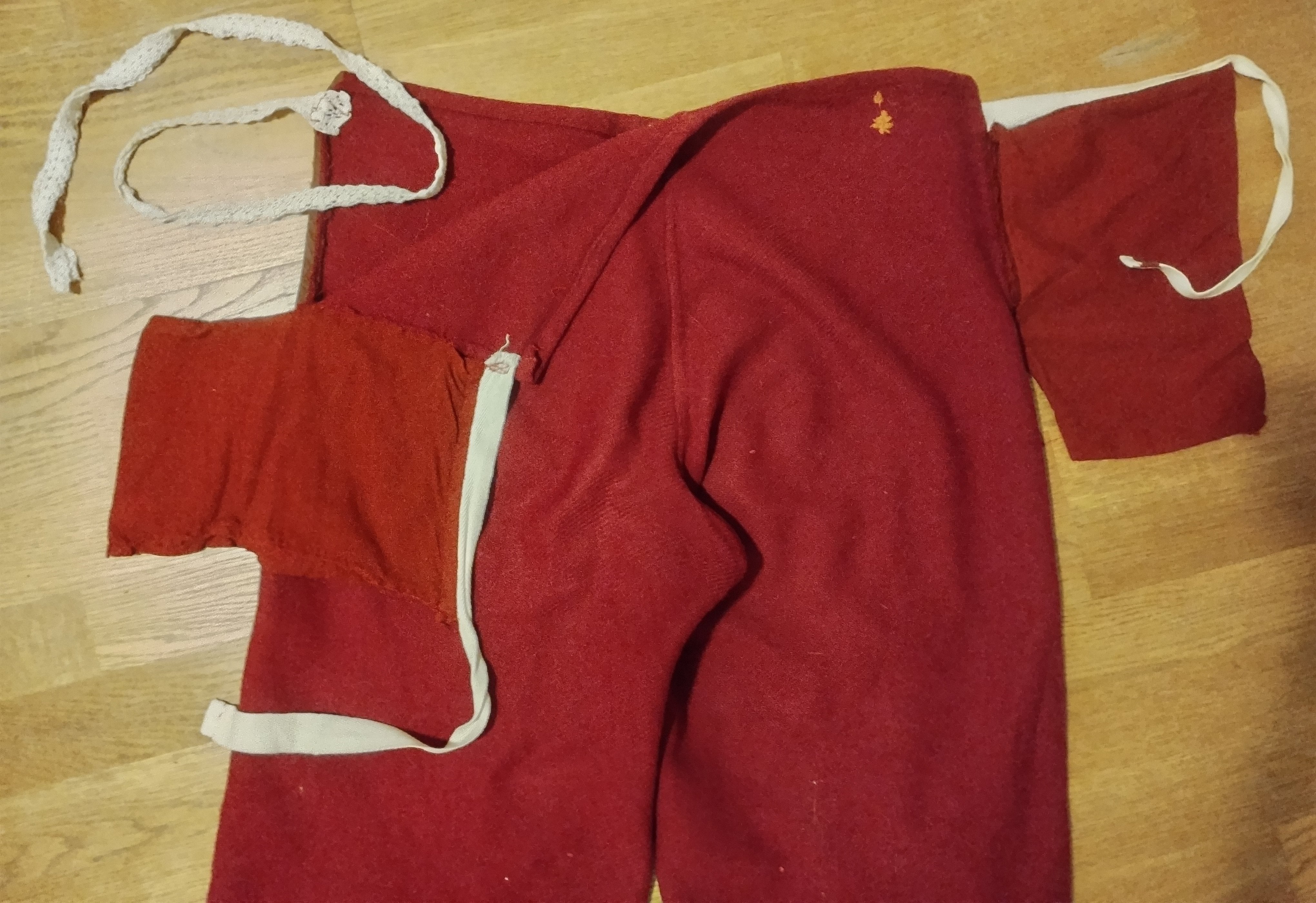 Red trousers laid flat, showing two separate waistband tabs on white cotton tape at each hip