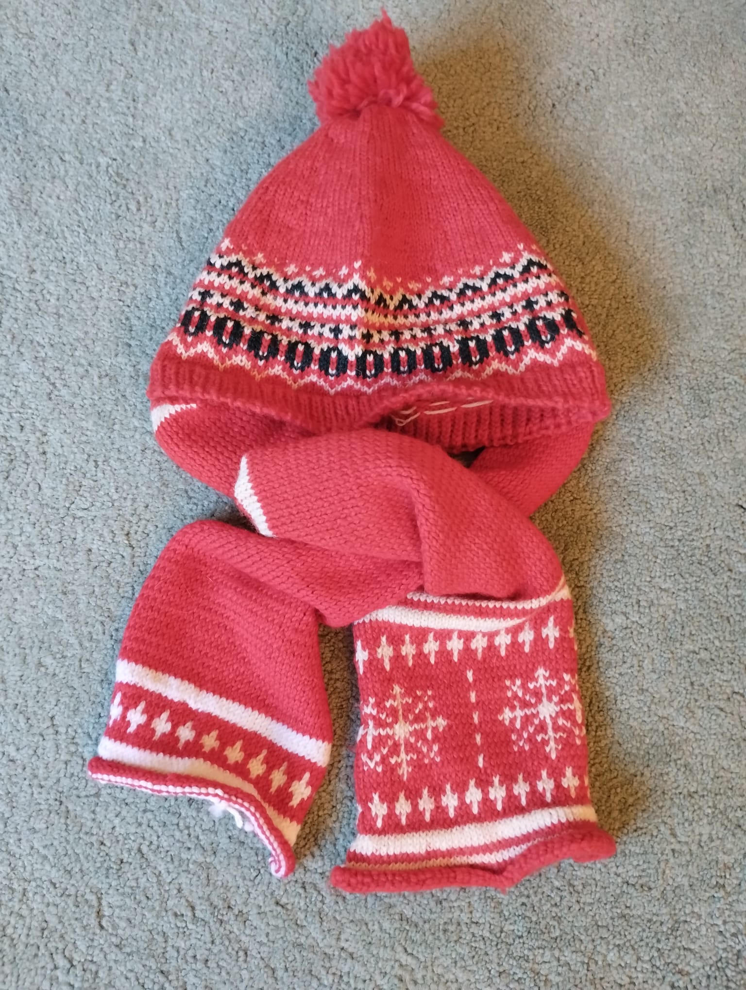 A red knitted bobble hat and matching scarf with a white Nordic snowflake pattern