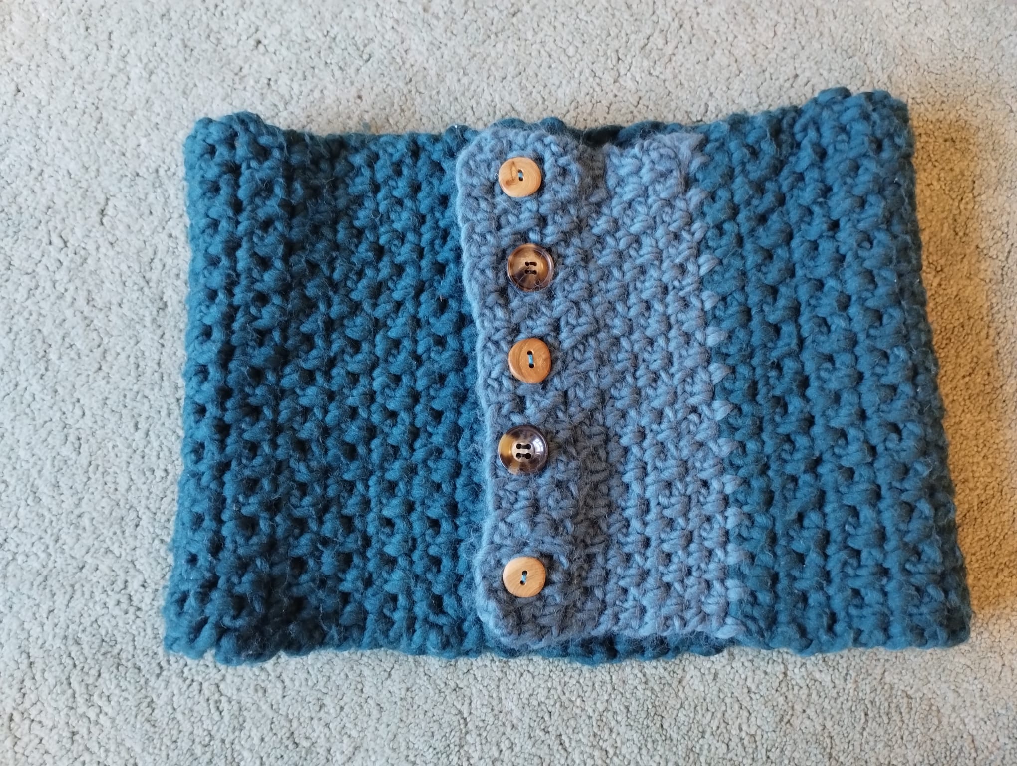 A teal crocheted cowl fastened with a row of wooden buttons