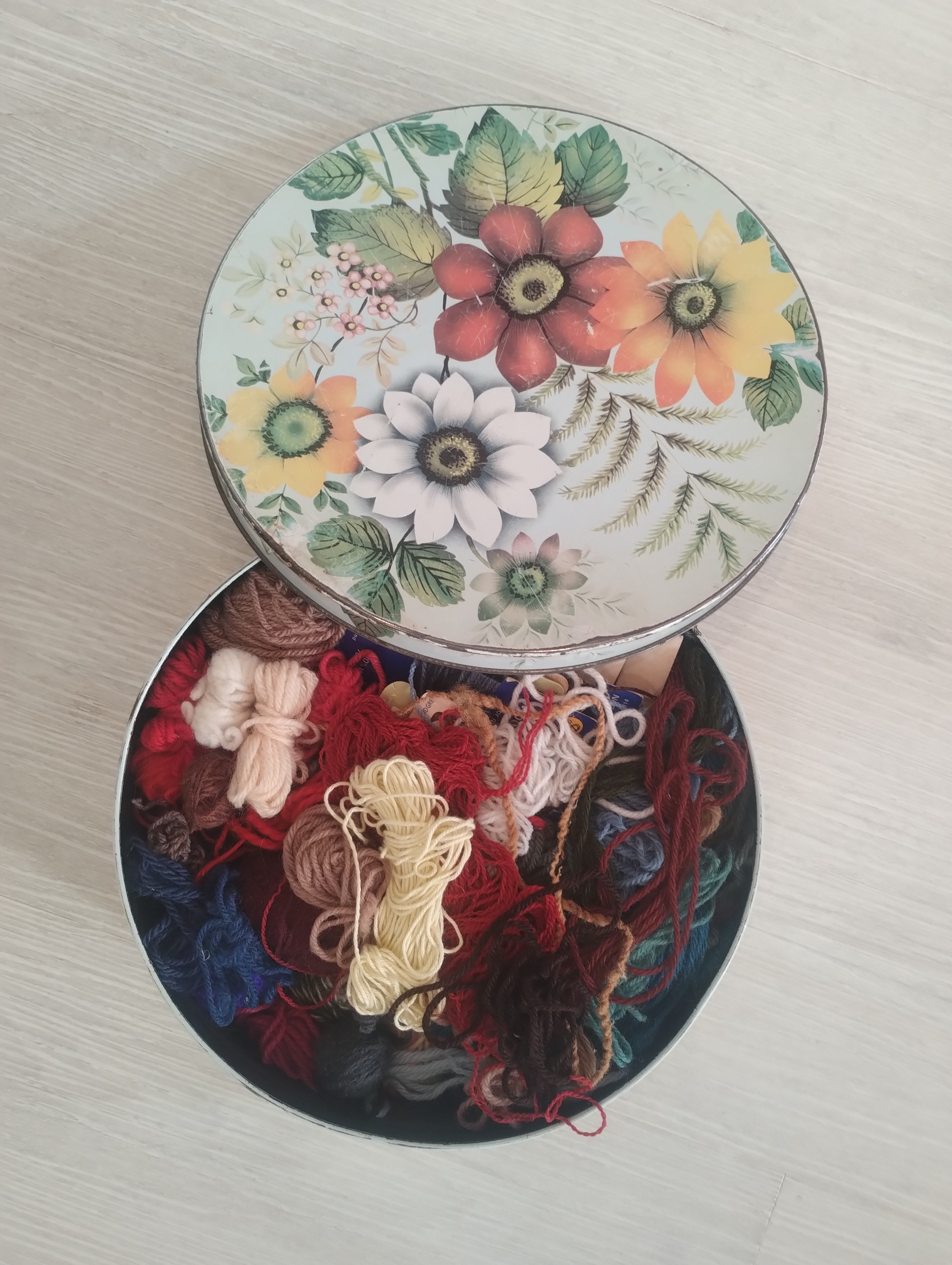 A floral tin full of oddments of leftover wool and embroidery thread