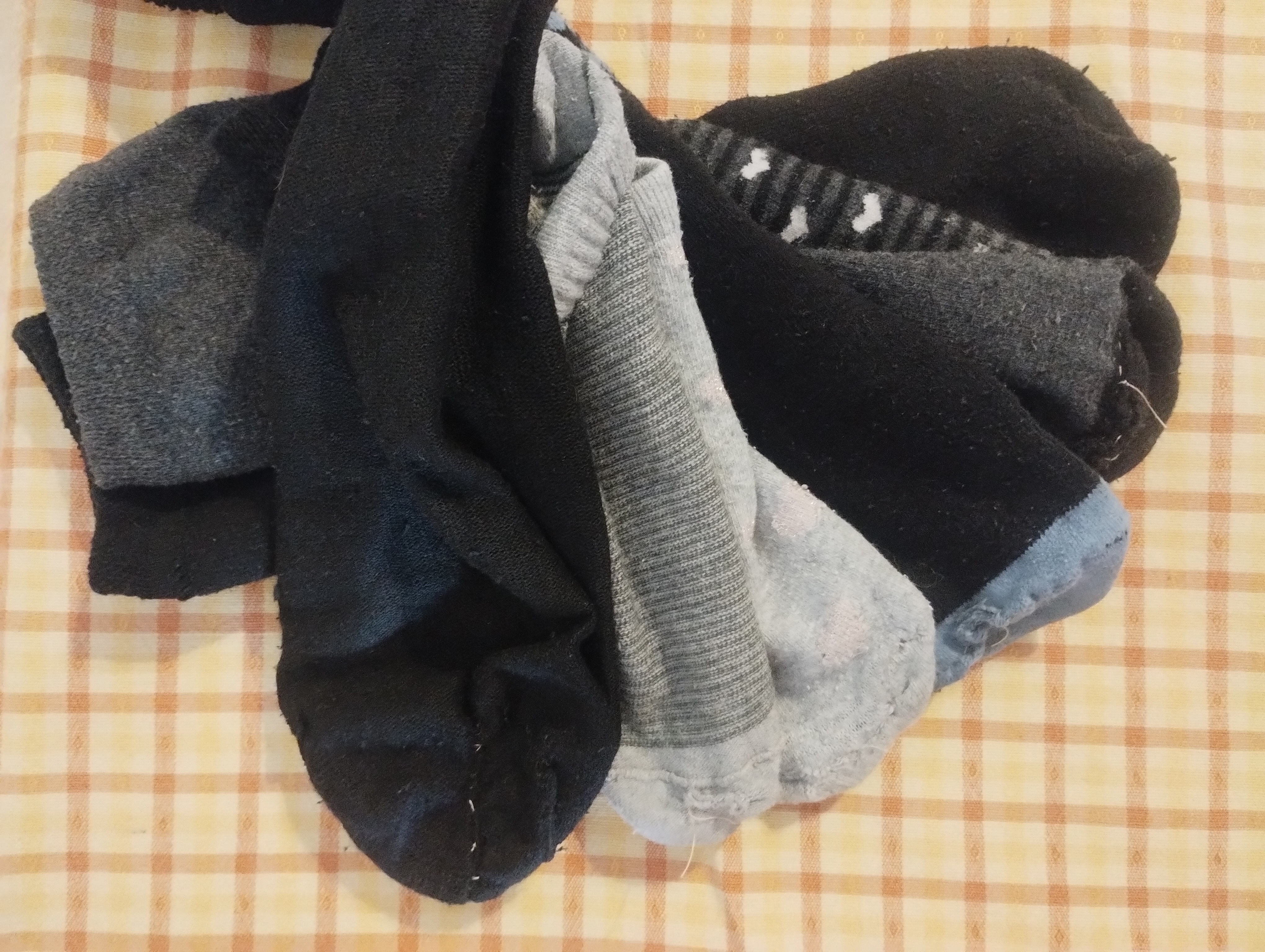 A pile of dark socks with pale contrasting thread visibly darning the heels and toes