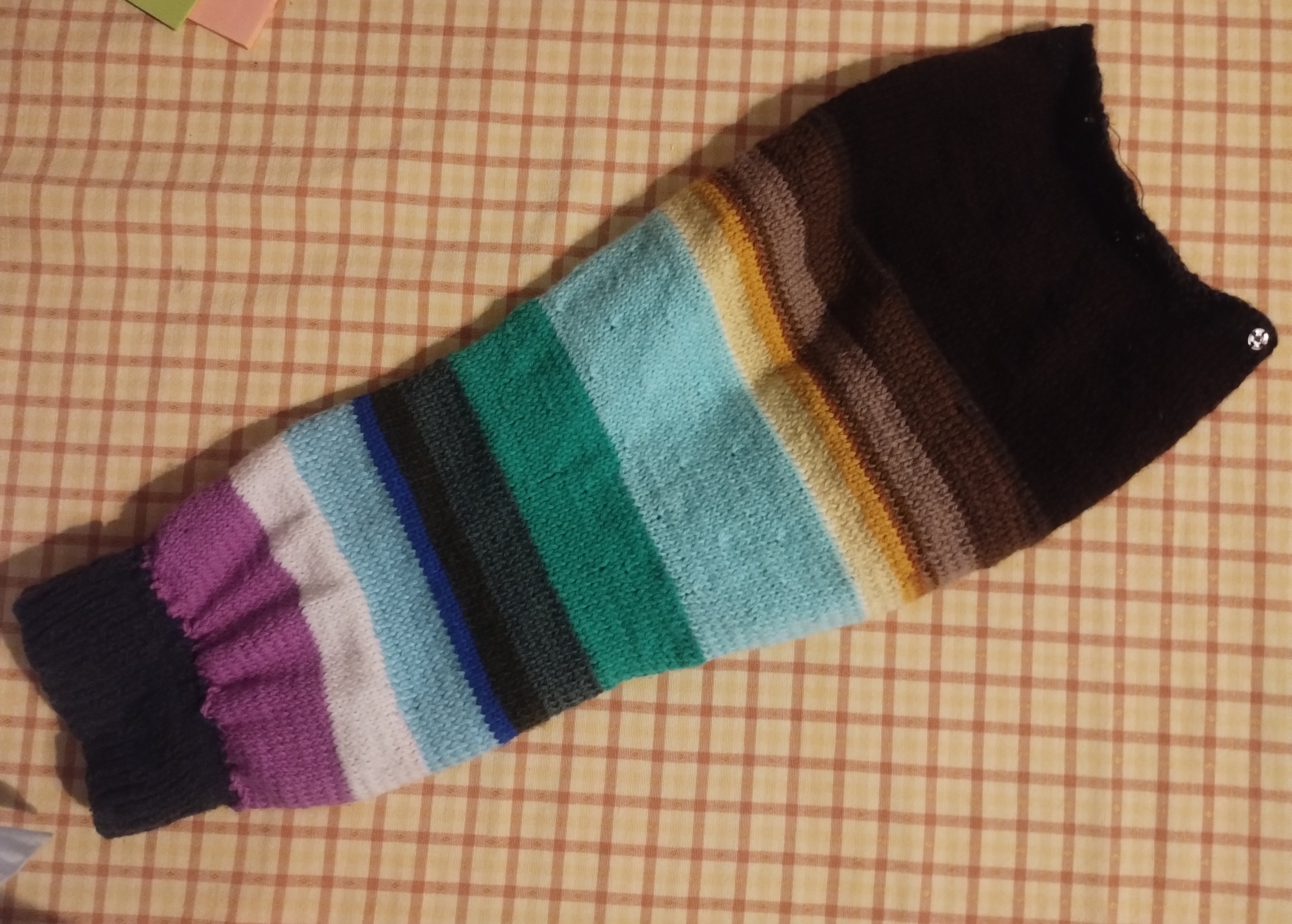 A long striped knitted panel shading from near-black through brown, teal, blue, and purple