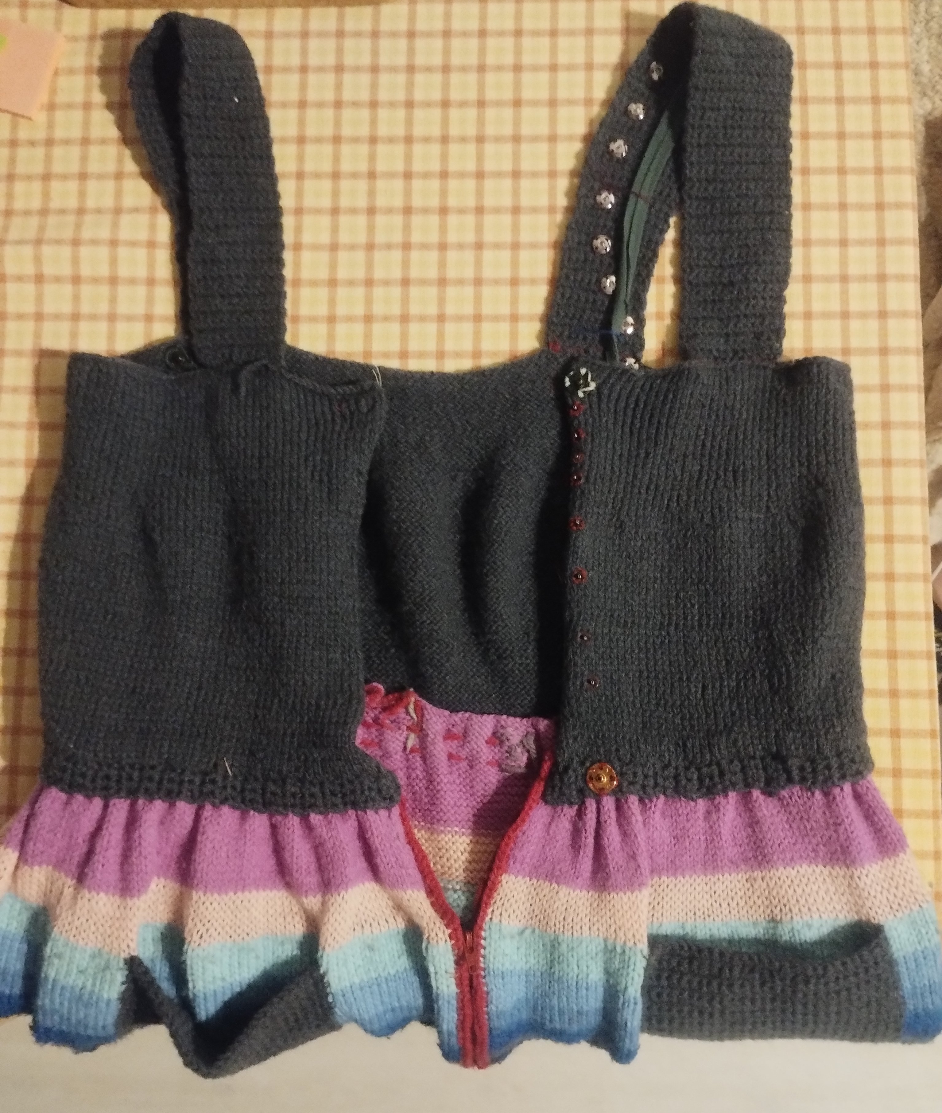 A striped knitted garment laid flat, showing a row of buttons and a pink ribbon tie at the waist