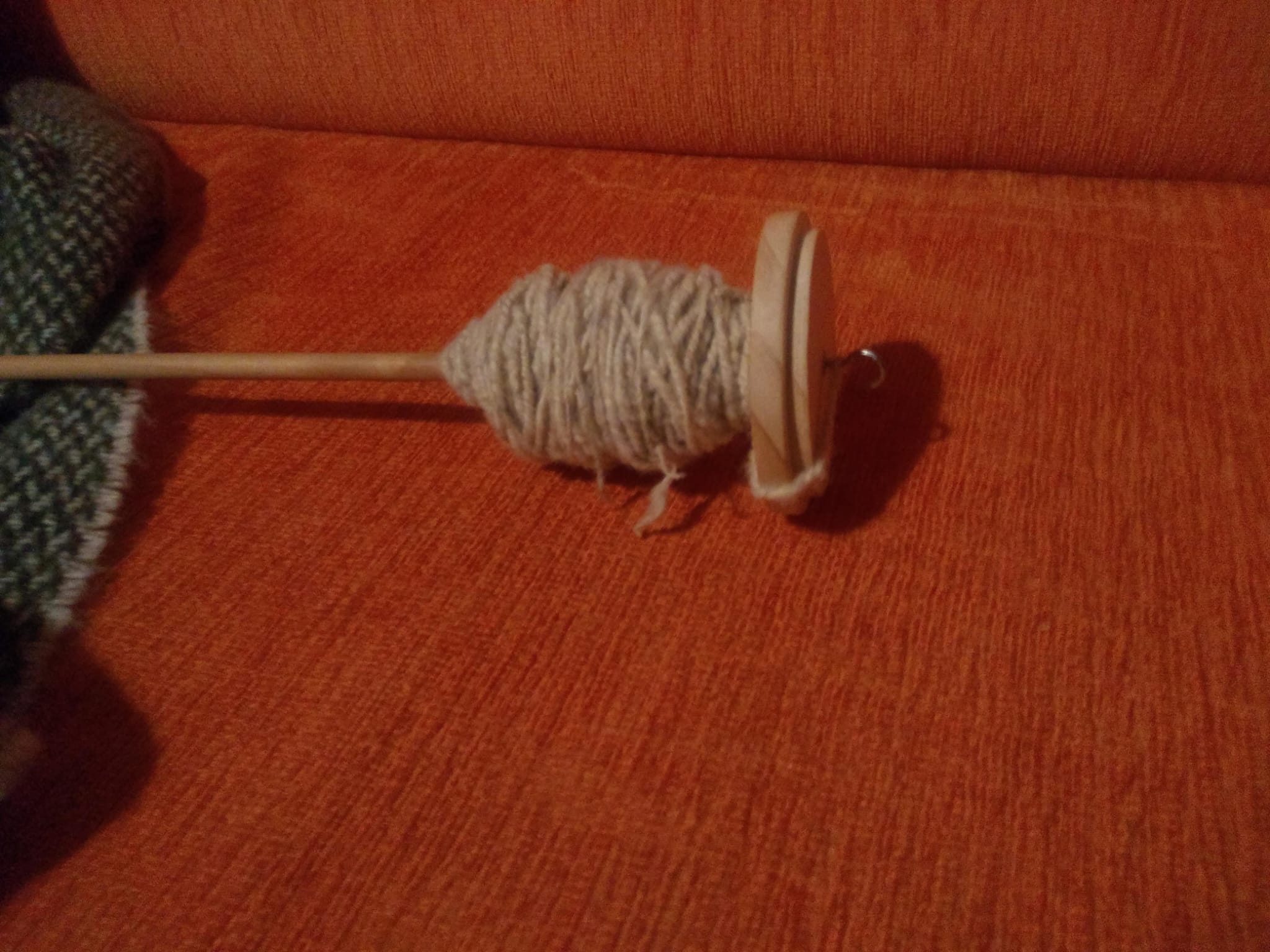 A hand spindle wound with pale handspun yarn, resting against a tweed project